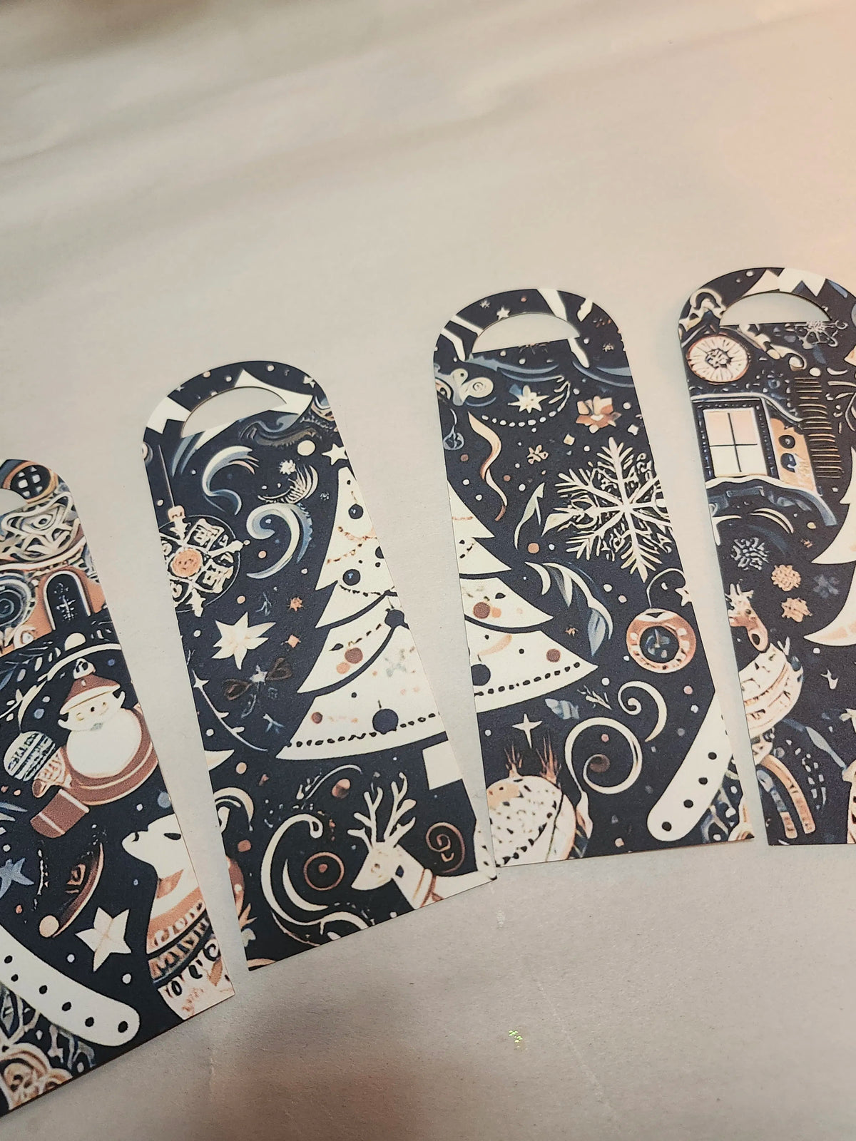 Five decorative bookmarks with a dark navy blue background and festive Christmas-themed illustrations, including Santa Claus, reindeer, snowflakes, stars, and a TARDIS, arranged on a light beige surface.