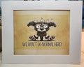 A framed art print featuring a cartoon illustration of a fluffy black and white dog with wide eyes and the text 'WE DON'T DO NORMAL HERE!' on a beige background, enclosed in a white frame.