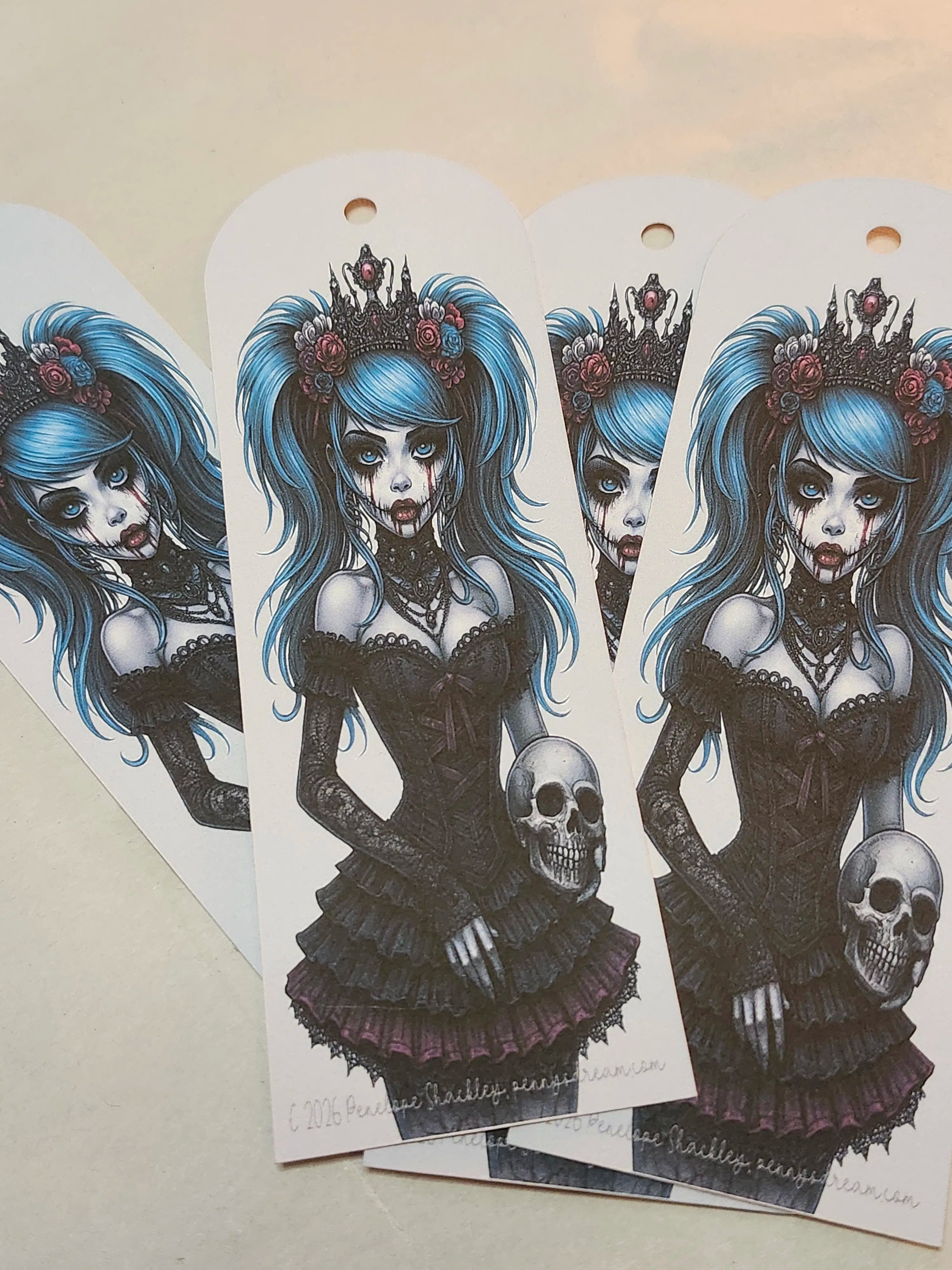 Three white arched bookmarks featuring a gothic zombie girl illustration with blue hair, a black dress, and a skull, displayed on a light beige surface.