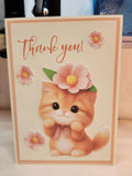 A handmade-style thank you card featuring a cute orange kitten illustration with a pink flower crown, surrounded by pink flowers and the text 'thank you!' in brown script, set against a cream background with a peach border.