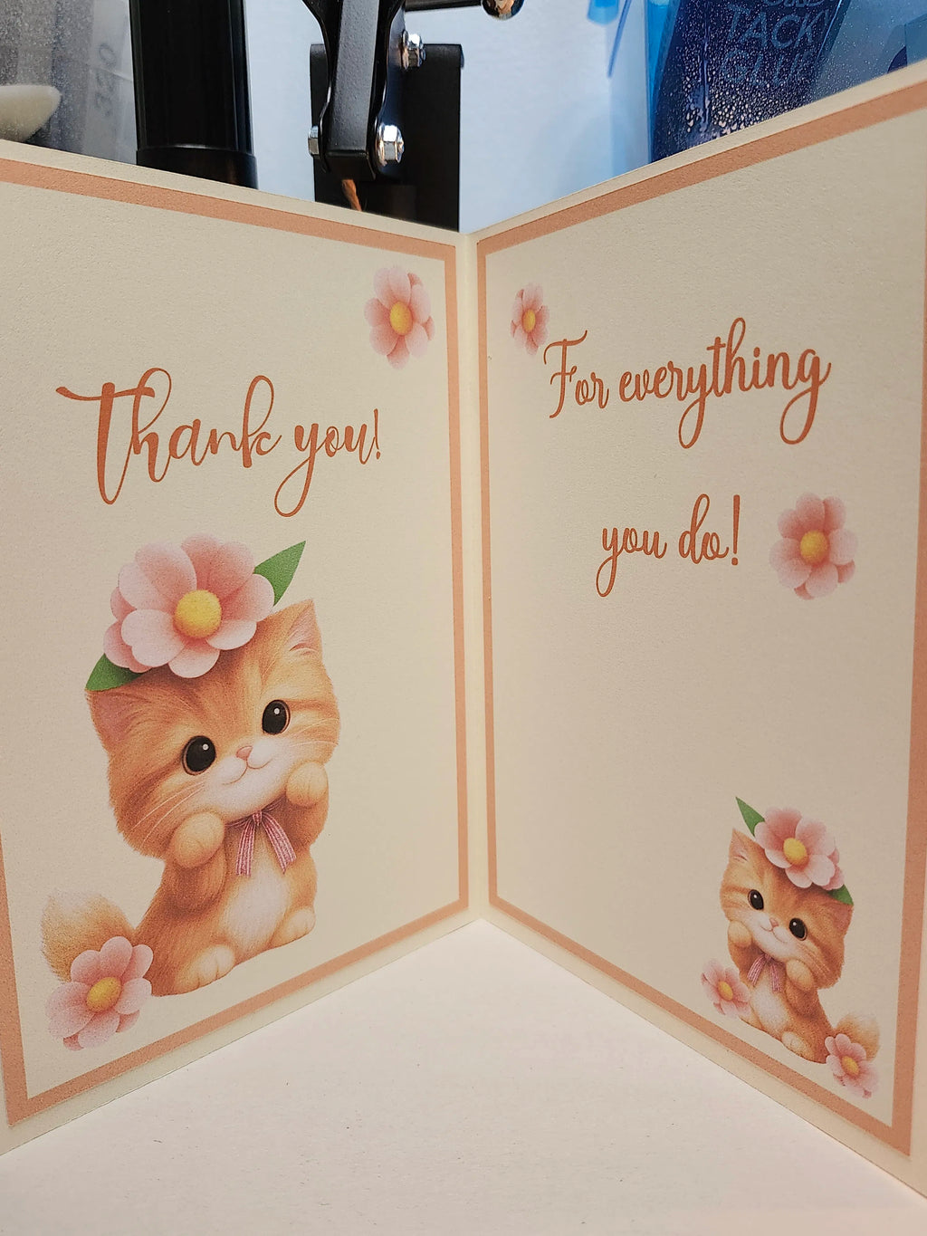 A folded greeting card or gift box insert shown open, with cream panels, peach borders, and cute orange kitten illustrations wearing pink flower crowns. One panel reads “Thank you!” and the other reads “For everything you do!”.