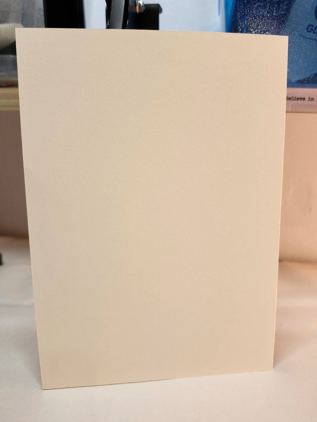 A plain, unprinted off-white card or sheet of paper standing upright on a light surface, photographed indoors with a blurred background.