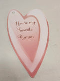 A heart-shaped paper tag with a small hanging hole, featuring the phrase 'You're my Favorite Human' in rose-gold cursive text over a soft pink and white gradient background.