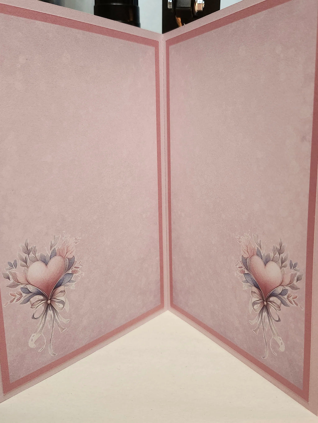 Pink cardstock craft paper with a textured pattern, featuring a pink border and a heart-shaped floral bouquet illustration in the bottom corners.