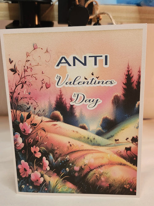 A square greeting card with a white border featuring a colorful landscape illustration and the text 'ANTI Valentines Day' in stylized lettering.