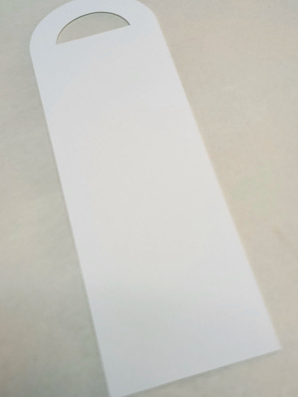 A blank white rectangular card with a rounded top and a small semicircular cutout, photographed on a light beige surface.