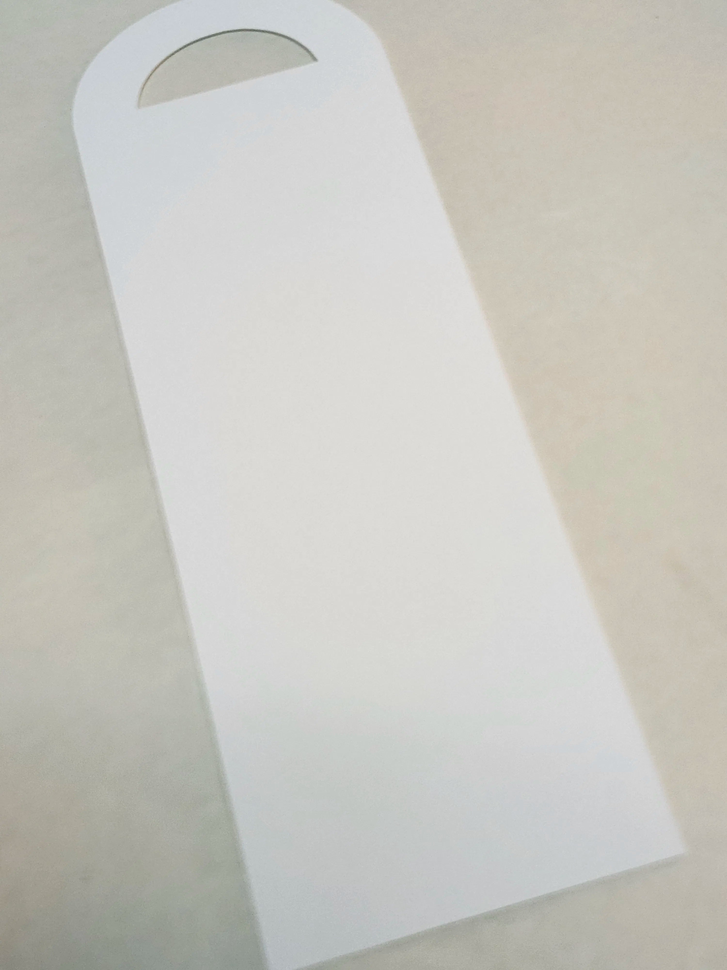 A blank white rectangular card with a rounded top and a small semicircular cutout, photographed on a light beige surface.