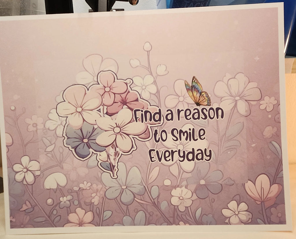 A square art print or card featuring the quote 'Find a reason to smile everyday' in dark brown lettering, surrounded by delicate floral illustrations in soft pink, lavender, and white tones, with a small butterfly on the right side.