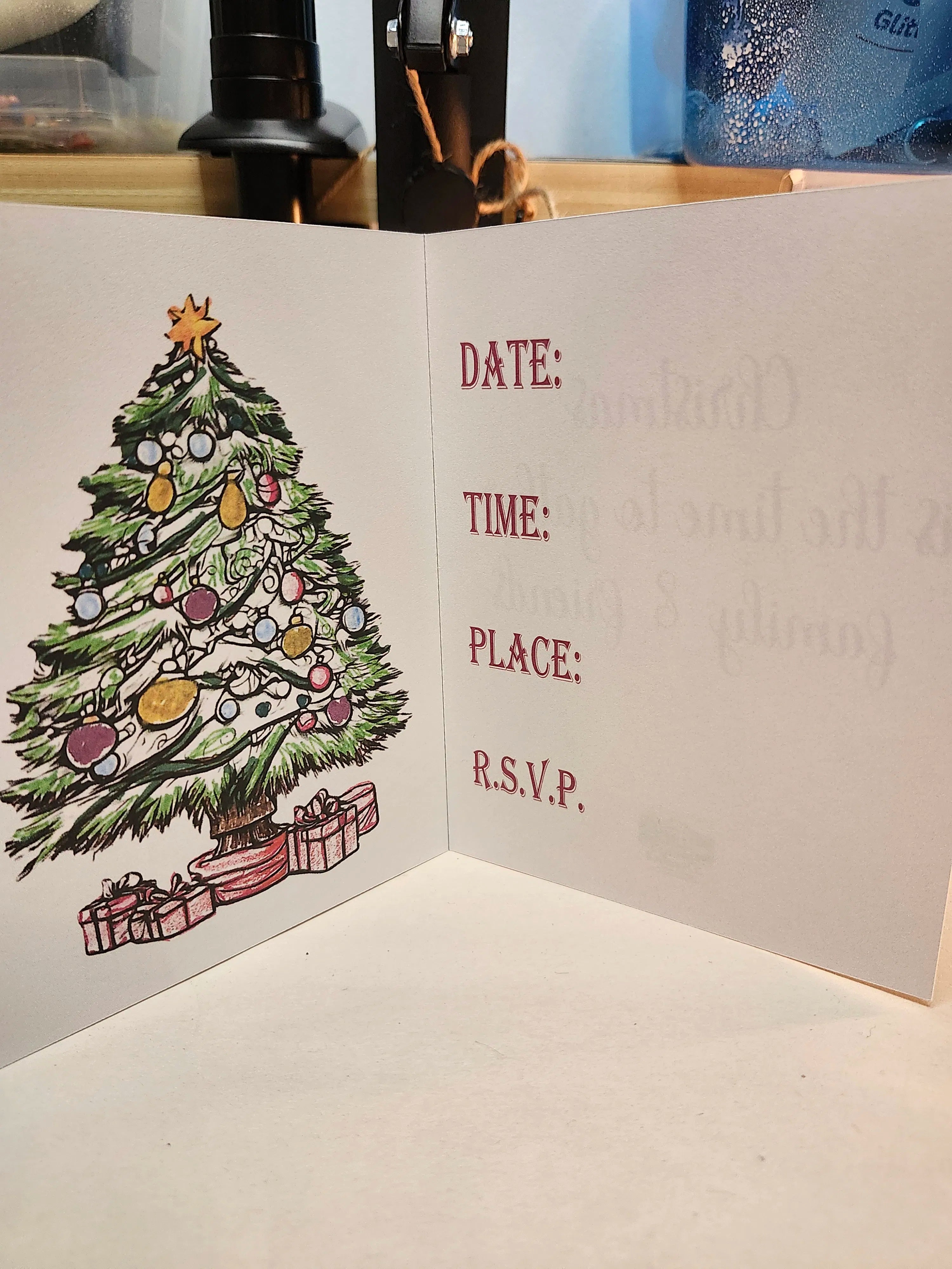An open white greeting card with a hand-drawn Christmas tree and presents on the left panel and blank fill-in lines for Date, Time, Place, and R.S.