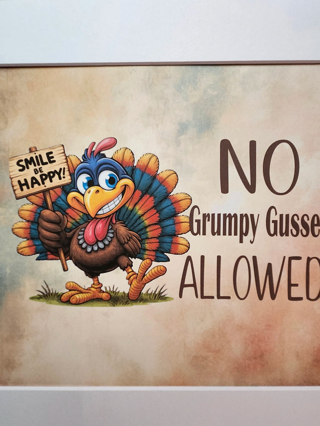 A framed Thanksgiving-themed wall sign with a cartoon turkey holding a sign that says 'SMILE AND HAPPY!' and the text 'NO Grumpy Gusse ALLOWED' on a mottled beige background.