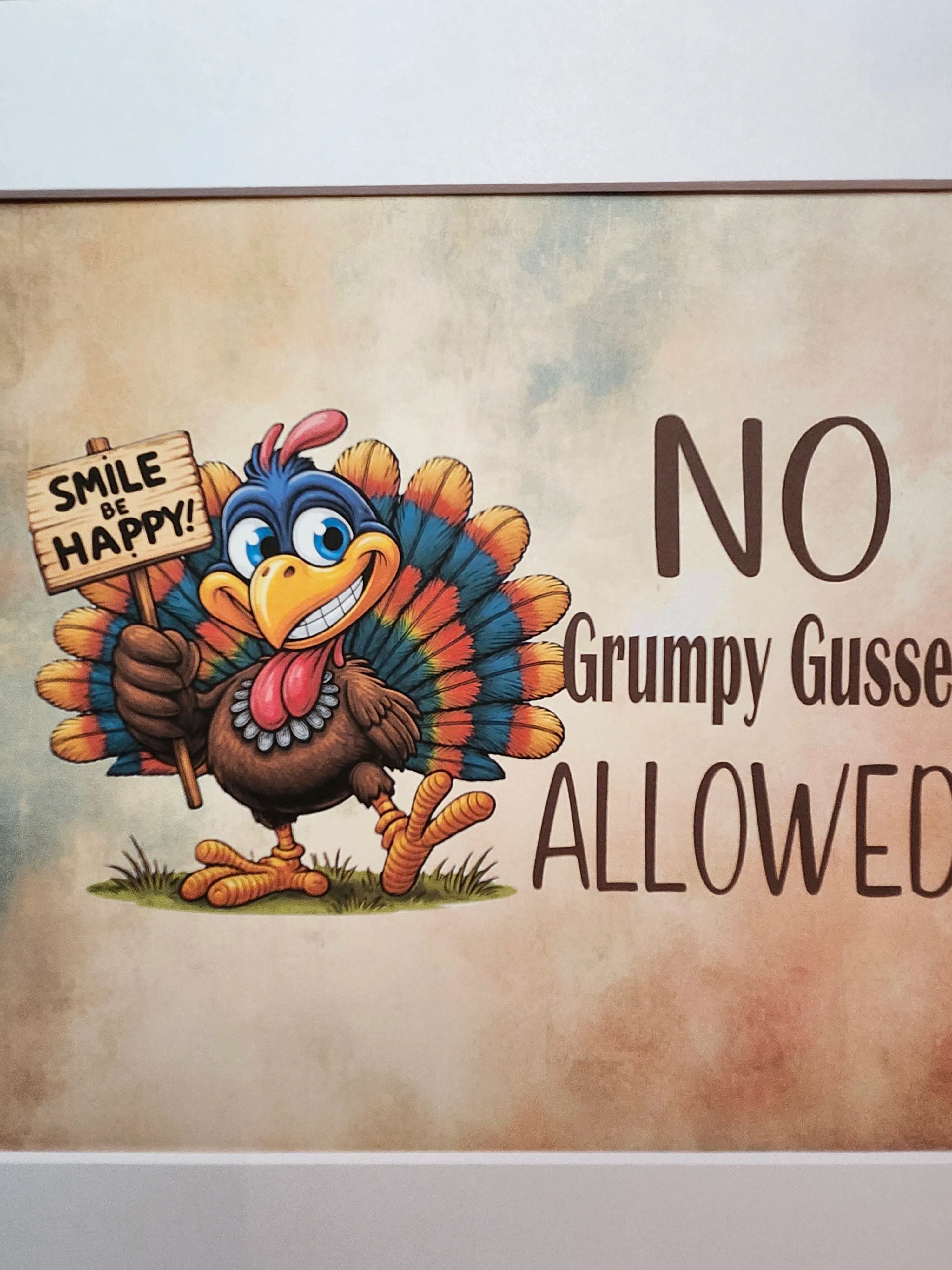 A framed Thanksgiving-themed wall sign with a cartoon turkey holding a sign that says 'SMILE AND HAPPY!' and the text 'NO Grumpy Gusse ALLOWED' on a mottled beige background.
