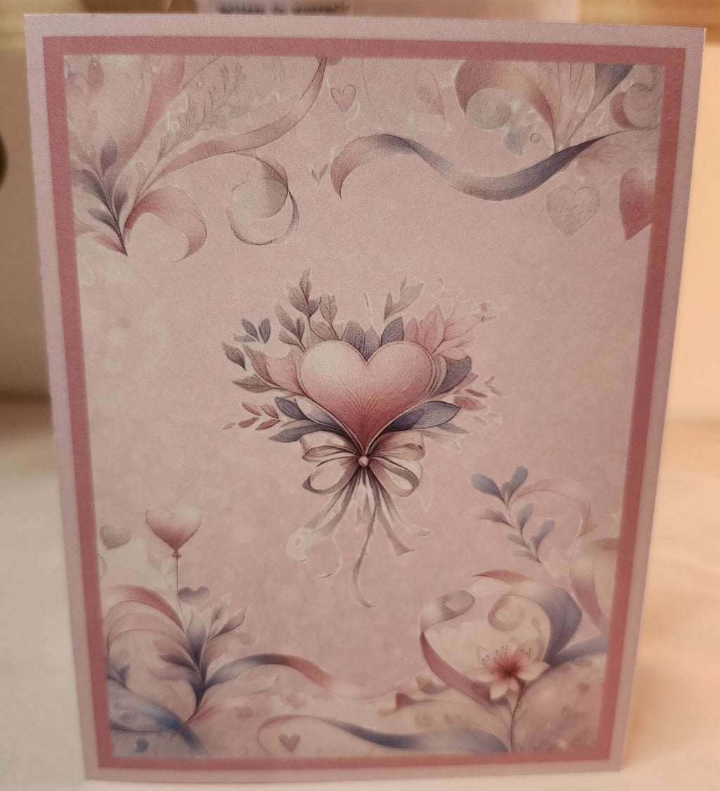 A square greeting card with a pink border and a central heart illustration surrounded by delicate floral and ribbon designs in soft pink, gray, and blue tones.