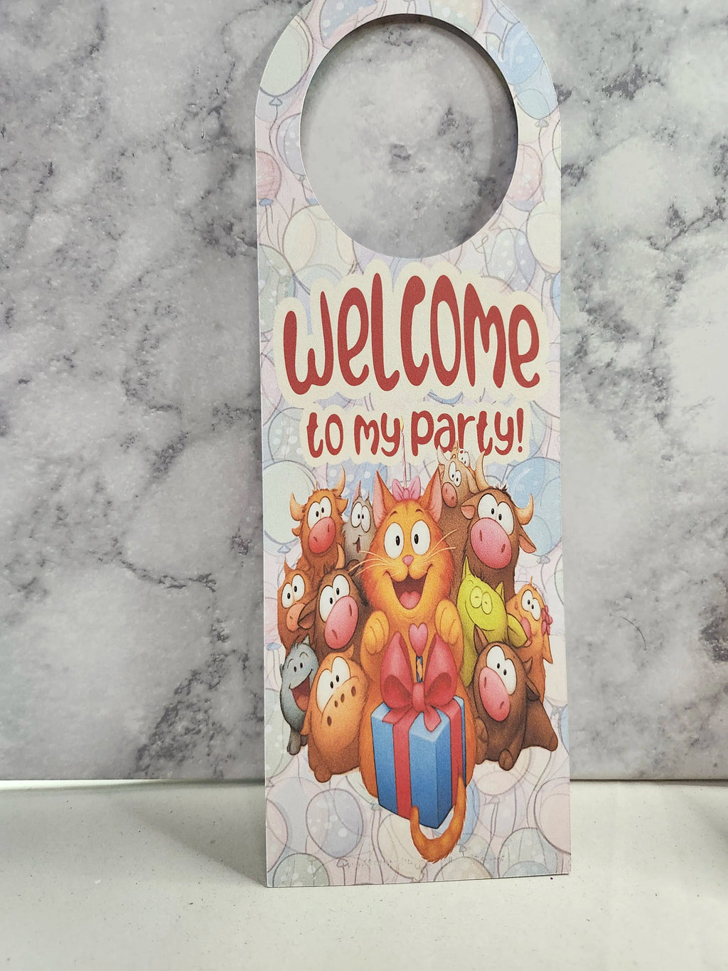 A novelty hanging door hanger with a cartoon cat and other party animals holding a gift box, with the text 'Welcome to my party!' in red, shown against a marble-patterned background.