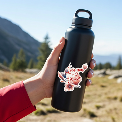 Person holding a black water bottle with a floral design and 'Love you forever' text against a mountainous background.