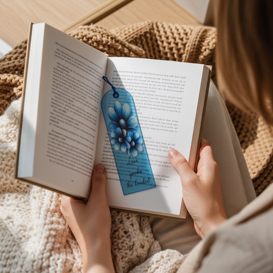 Person holding an open book with a blue bookmark featuring blueberries.