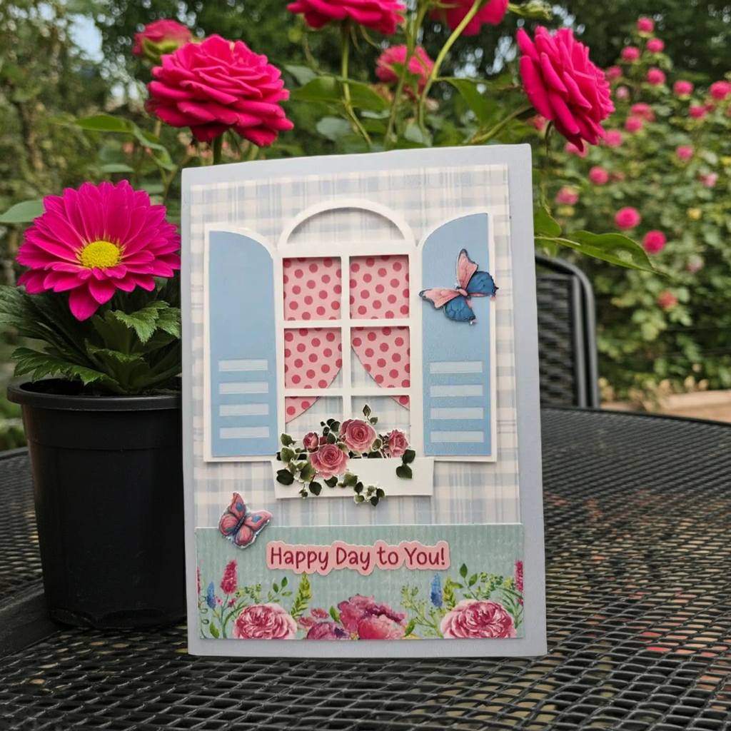 Decorative card with floral design and 'Happy Day to You!' text, placed on a table with pink flowers in the background.